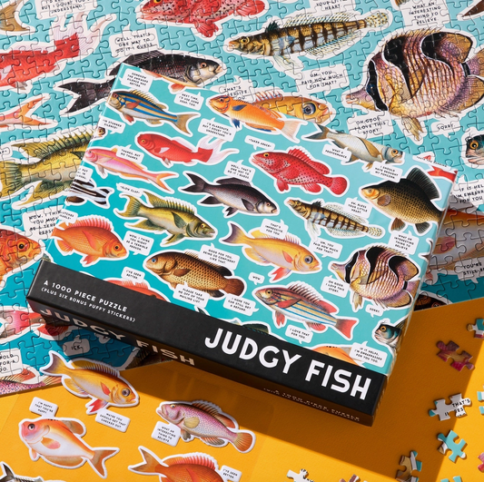 Jigsaw puzzle with fish illustrations and a box labeled 'Judgy Fish' on a yellow surface.