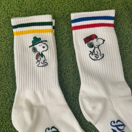 Two white socks with embroidered snoopy designs on a green background