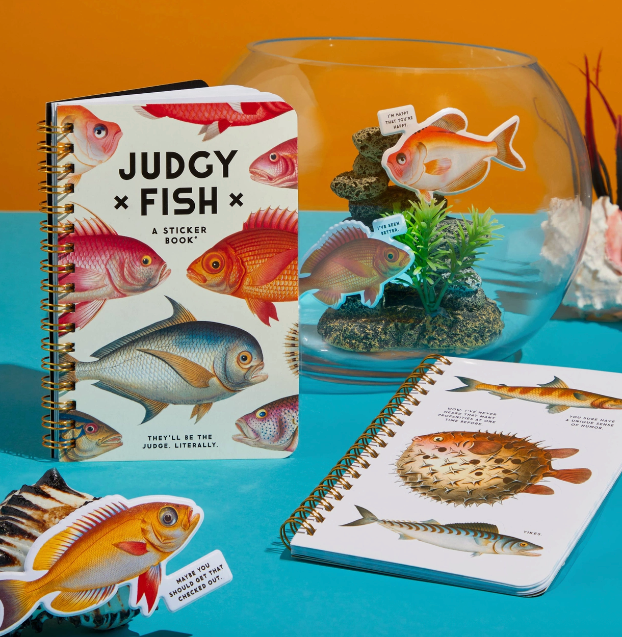 Book of fish stickers with fish illustrations and a fishbowl with decorative fish on a blue surface.