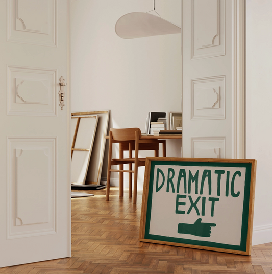 Framed sign with 'Dramatic Exit' text in a room with wooden floor and white walls.