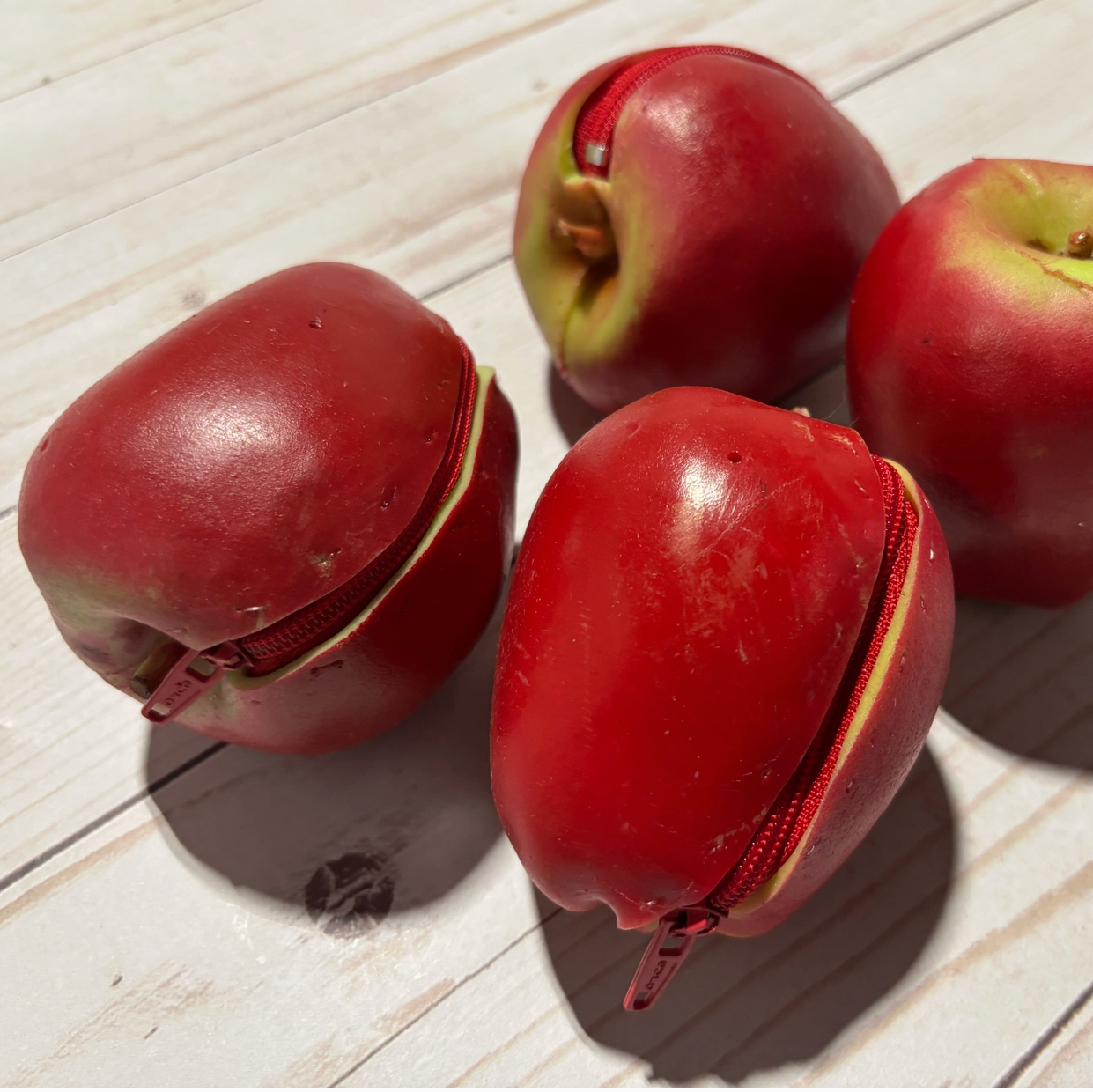 Four red and green apple coin purses on a light wooden surface