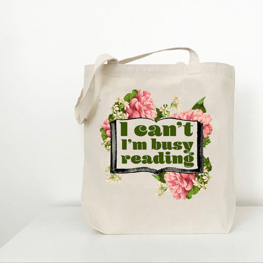 Tote bag with floral design and text 'I can't I'm busy reading' on a white background