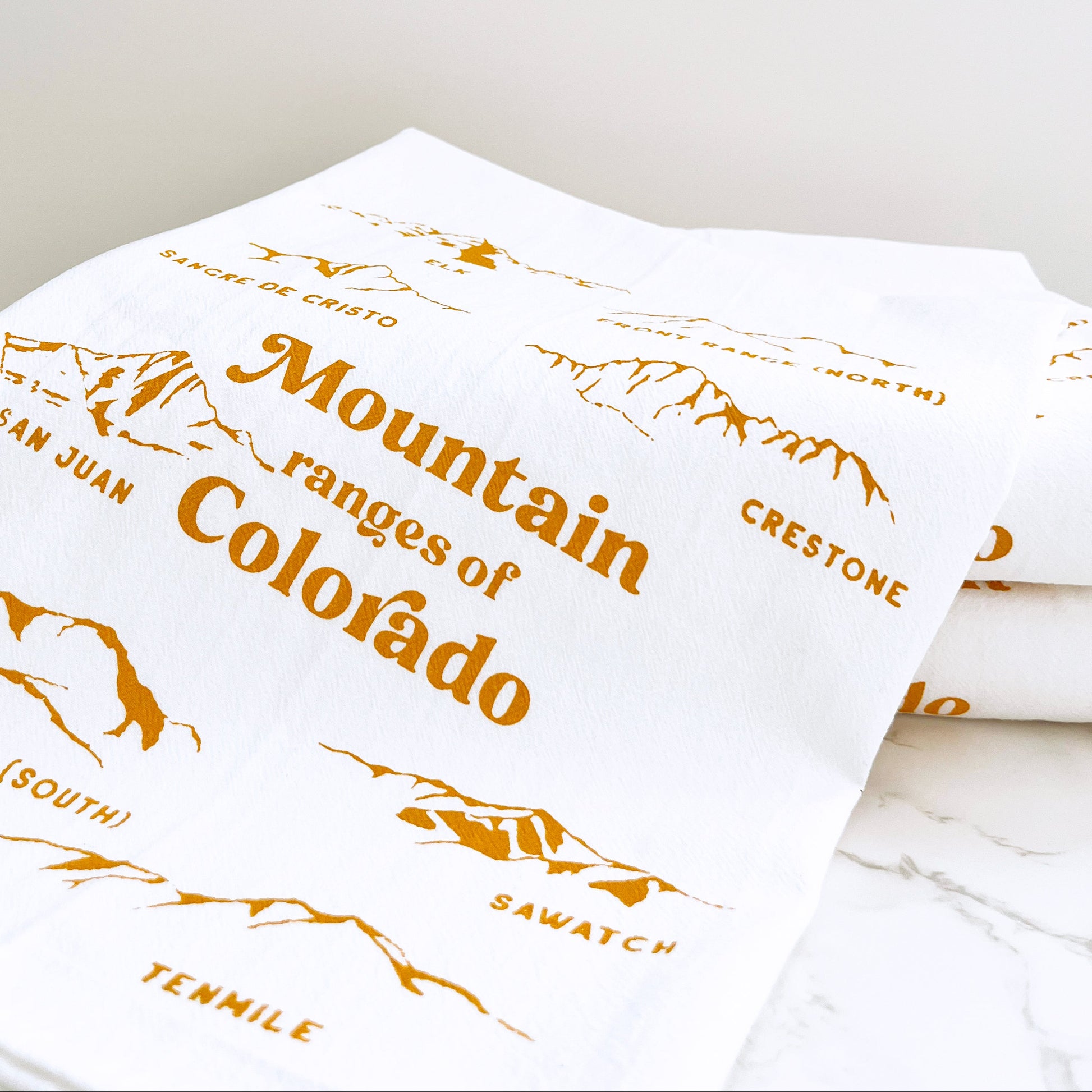 White kitchen towel with yellow colorado text and mountain range illustration on a white background