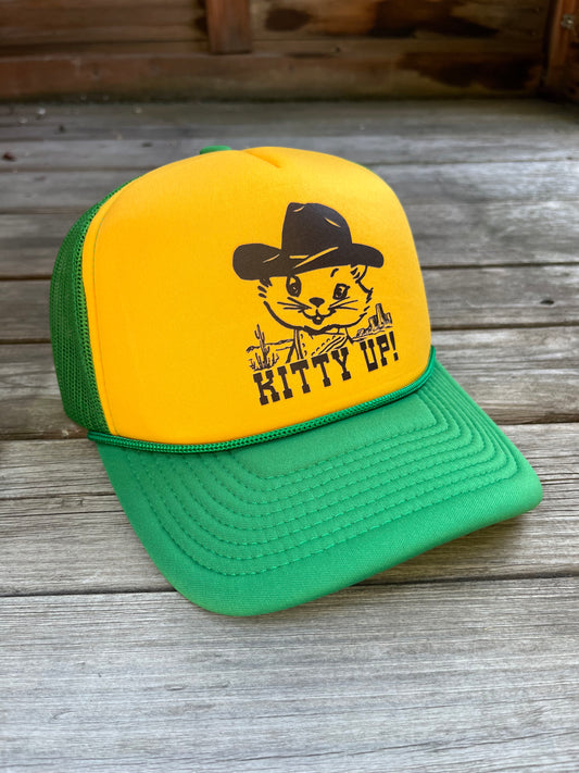 Yellow and green cap with a cat graphic and 'Kitty Up!' text on a wooden surface
