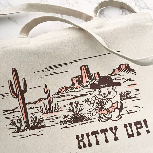 Tote bag with desert scene and cat illustration, featuring the text 'Kitty Up!'.