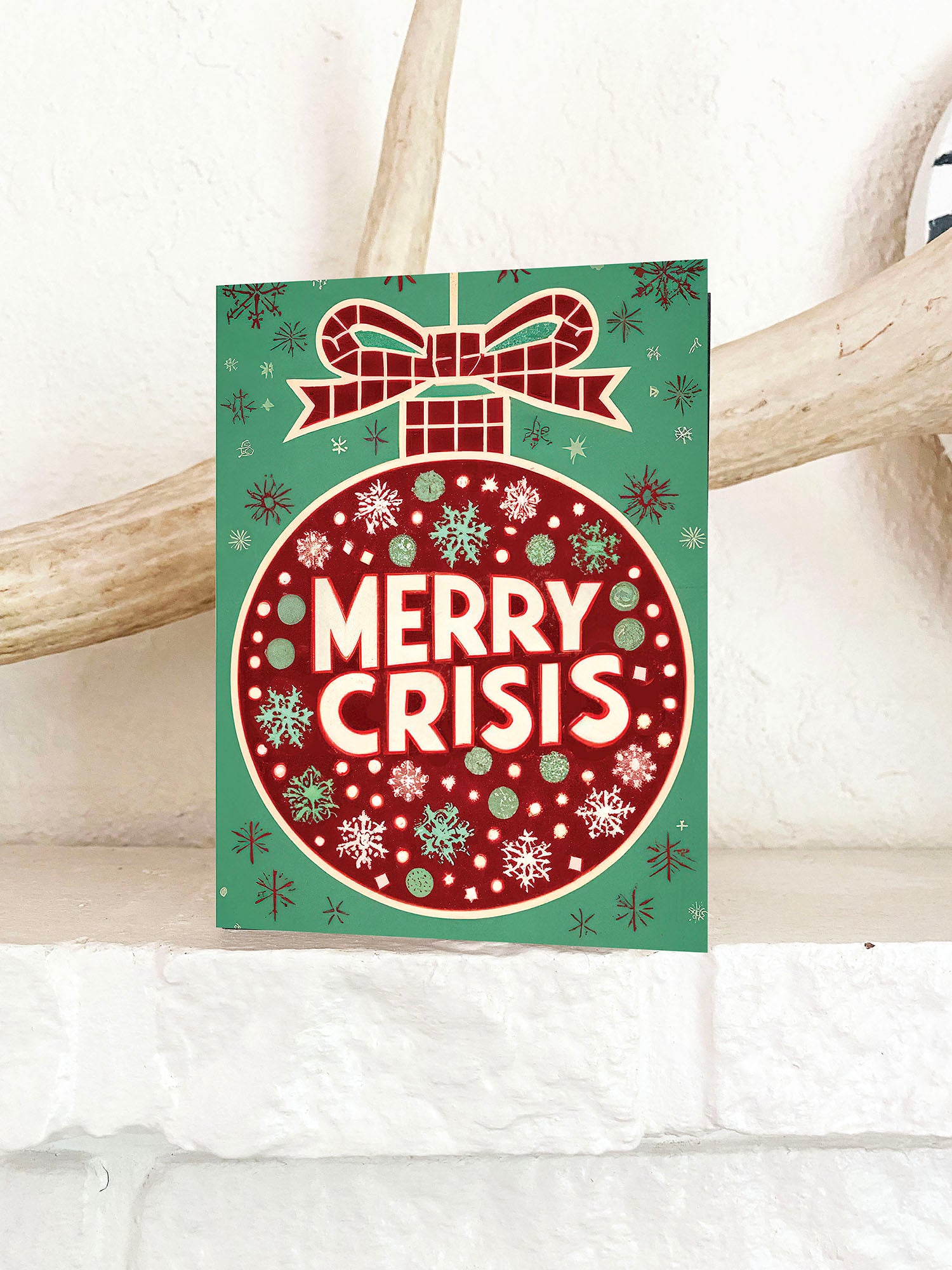 Red ornament on a green background with “Merry Crisis” text and snowflakes.