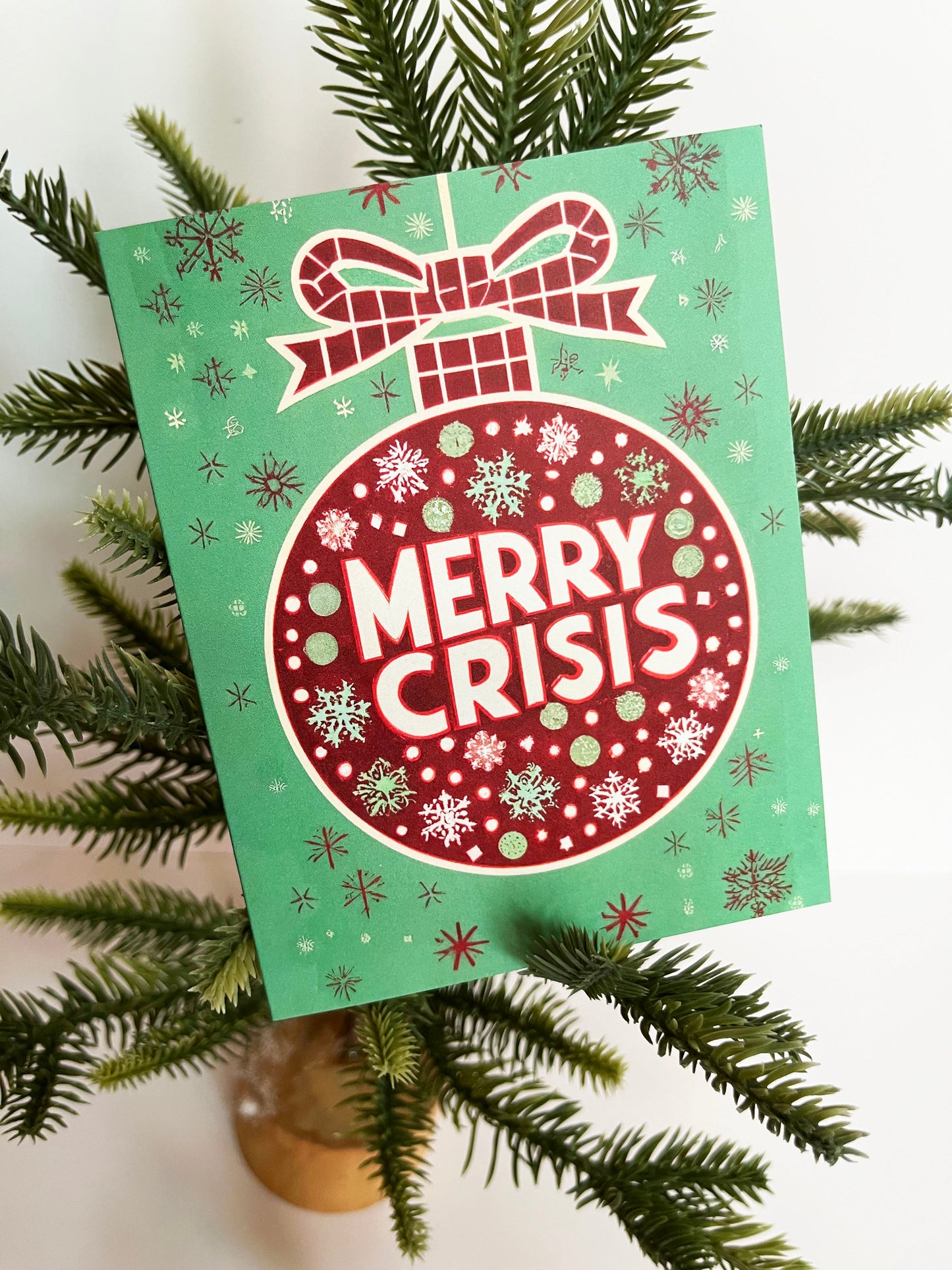 Red ornament on a green background with “Merry Crisis” text and snowflakes.