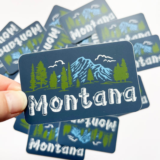 Montana-themed stickers with mountain and tree design held by a hand on a white background