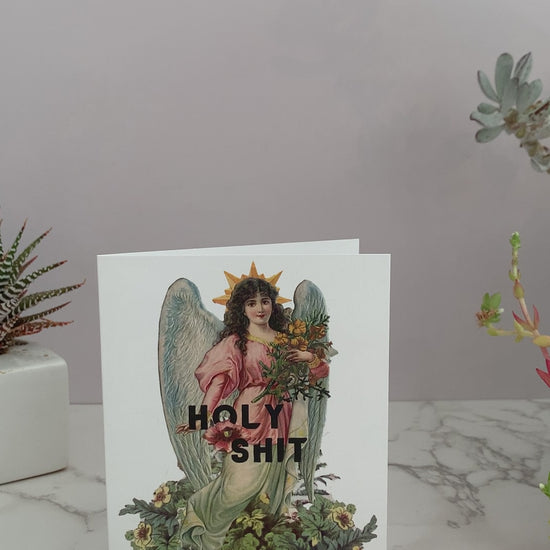 All purpose greeting card perfect for any occasion, like birthdays, celebrations, or just because. White card that features a vintage angel with flowers. Greeting says, "Holy Shit." Vintage colors of pinks, blues, greens, and yellows. Blank inside