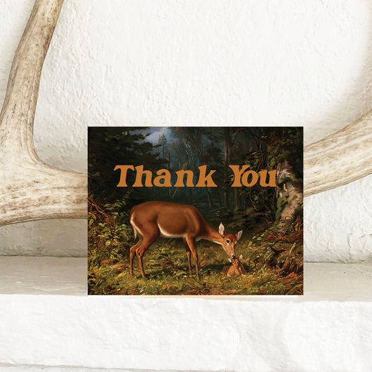 Card with deer illustration and 'Thank You' text on a wooden surface with antlers.